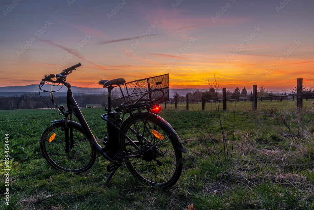 Fototapeta premium Black electric bicycle with sunset on light green meadow in spring evening