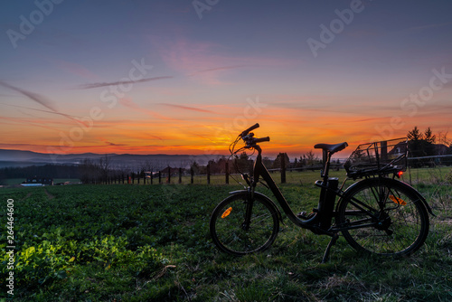 Black electric bicycle with sunset on light green meadow in spring evening