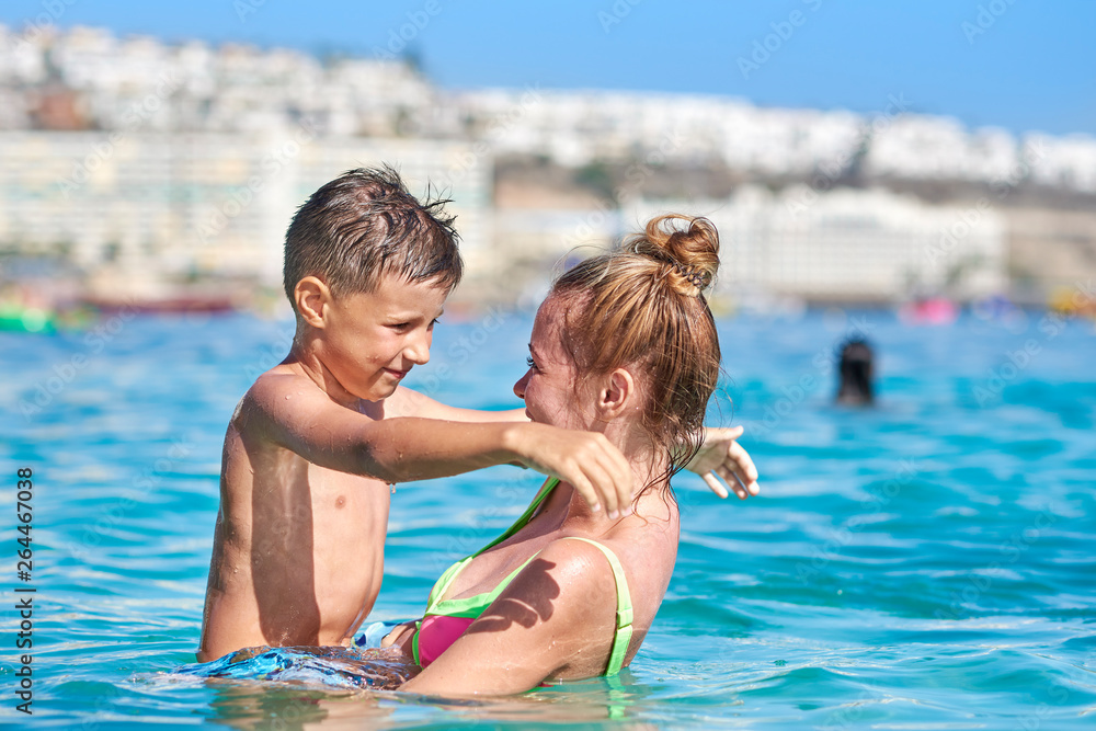 Mom and son are having fun during their summer holidays, they are swimming in the ocean, smiling and hugging each other. Mom and son are having fun during their summer holidays, they are swimming in the ocean, smiling and hugging each other.
