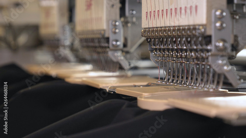 In slow motion video in a garment factory, a sewing machine embroiders various companies and engravings. Concept of: Automated work, Sewing machine, Engraving, Thread, Fabric, Needle.