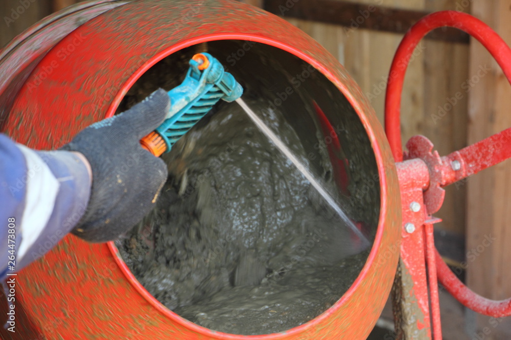 Worker washes red concrete mixer with a stream of water