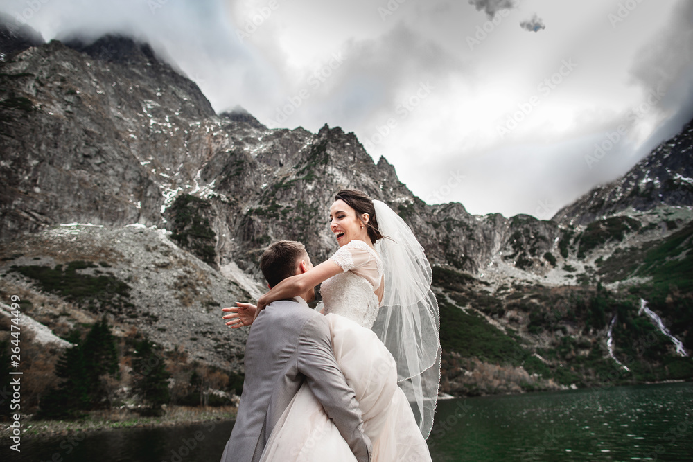 Naklejka premium Beautiful wedding photosession. The groom circles his young bride, on the shore of the lake Morskie Oko. Poland