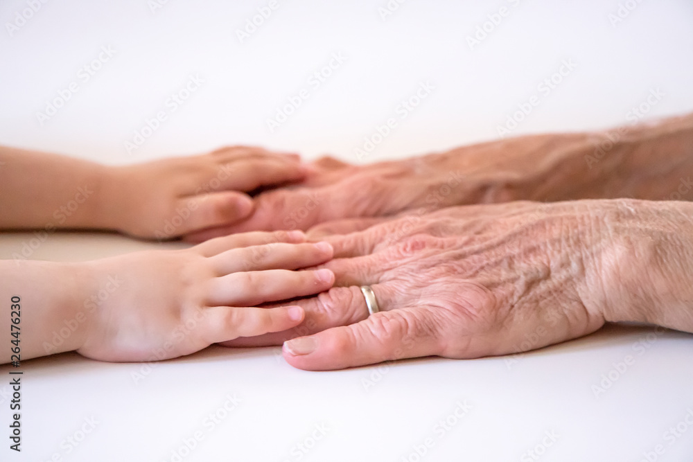 An elderly woman (old lady, grandmother) holds her little granddaughter's small hands. Family unity, love, help, assistance. Age and generational difference. Aged and wrinkled hands with young hands. An elderly woman (old lady, grandmother) holds her little granddaughter's small hands. Family unity, love, help, assistance. Age and generational difference. Aged and wrinkled hands with young hands.