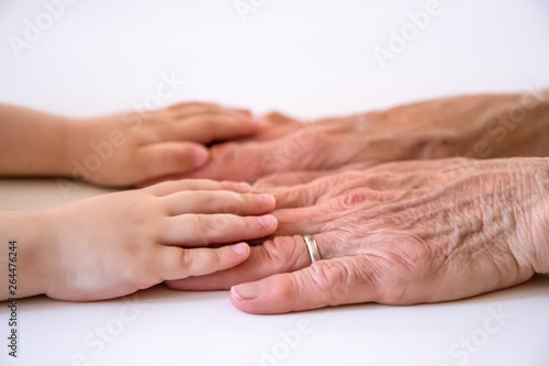 An elderly woman (old lady, grandmother) holds her little granddaughter's small hands. Family unity, love, help, assistance. Age and generational difference. Aged and wrinkled hands with young hands.
