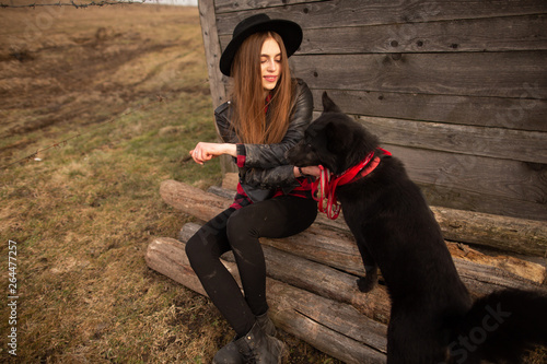 happy young woman sitting with her black dog in fron of old wooden house photo