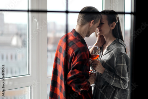 Young beautiful couple in plaid shirts on the balcony of a multistory building. Drink and taste wine, laugh and embrace. © spaskov