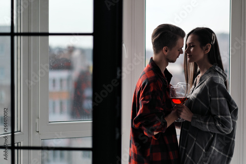 Young beautiful couple in plaid shirts on the balcony of a multistory building. Drink and taste wine, laugh and embrace.