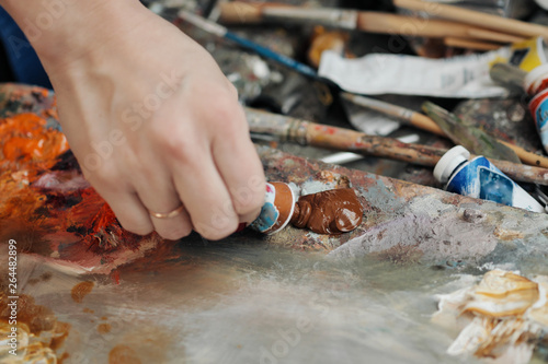 A woman artist squeezes oil paint onto a palette from a tube.