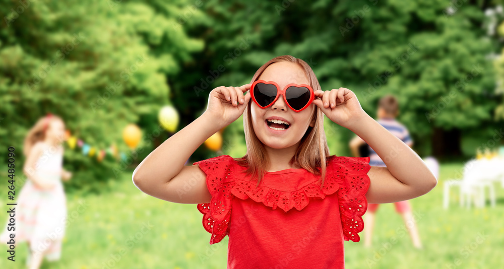 childhood, valentine's day and summer concept - happy preteen girl with heart shaped sunglasses over birthday party at park childhood, valentine's day and summer concept - happy preteen girl with heart shaped sunglasses over birthday party at park