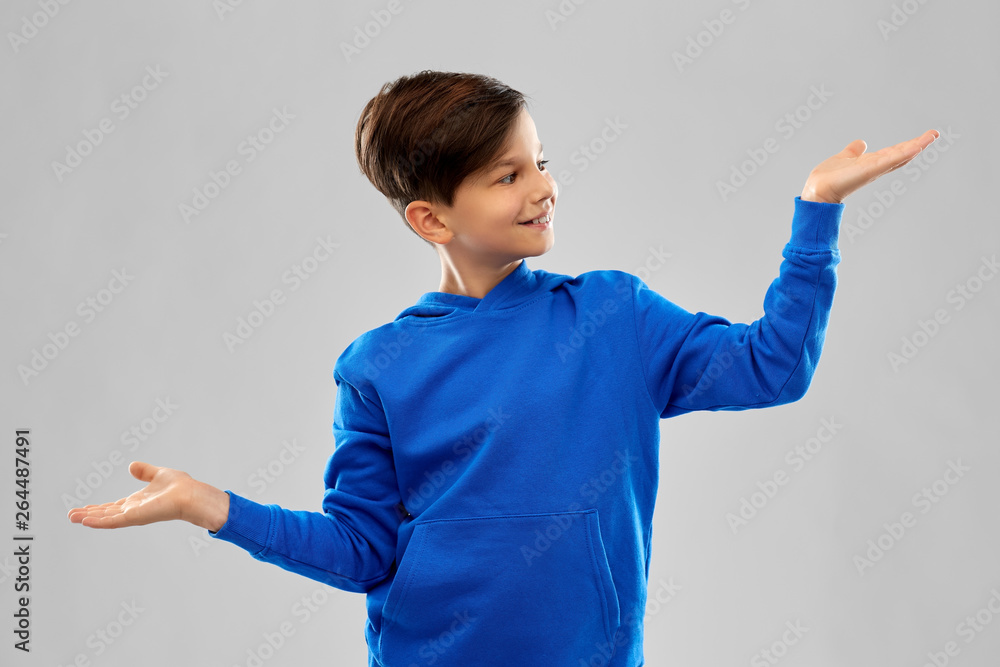 childhood, gesture and people concept - smiling boy in blue hoodie holding something imaginary on empty hands over grey background childhood, gesture and people concept - smiling boy in blue hoodie holding something imaginary on empty hands over grey background