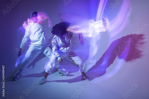 Young man and woman in sportswear performing energetic dance movements and leaving light traces under bright violet illumination photo