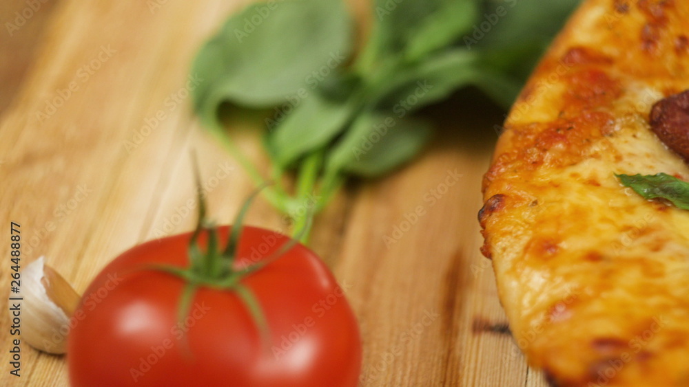 Fresh hot appetizing peperoni pizza lying on a wooden plate on the table decorated with basil greens, tomato and garlic in slow motion close up front view 4K video Fresh hot appetizing peperoni pizza lying on a wooden plate on the table decorated with basil greens, tomato and garlic in slow motion close up front view 4K video