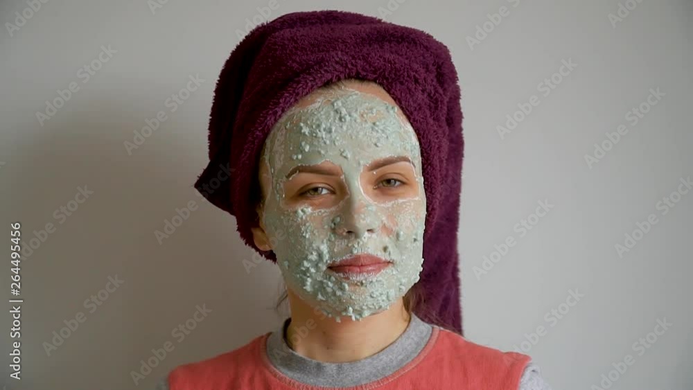 Woman with cosmetic green mask on her face looking at camera and smiles Woman with cosmetic green mask on her face looking at camera and smiles