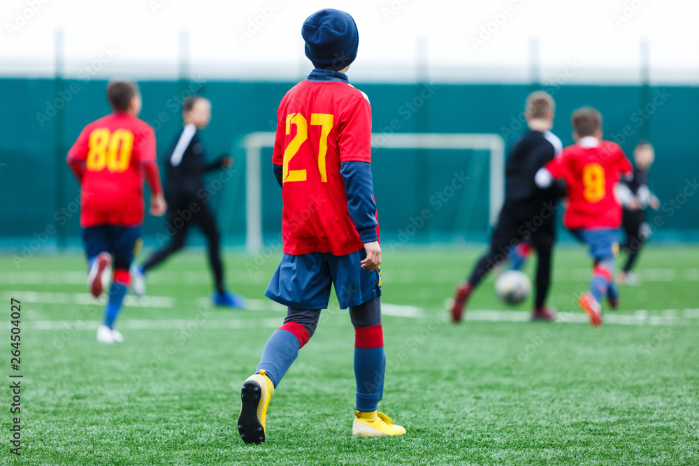 Obraz premium Boys kick soccer ball. Footballers run after the ball on green grass. Kids in white and red shirts dribbling, improve skills. Training, football, hobby, active lifestyle