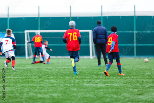 Boys kick soccer ball. Footballers run after the ball on green grass. Kids in white and red shirts dribbling, improve  skills. Training, football, hobby, active lifestyle © Natali