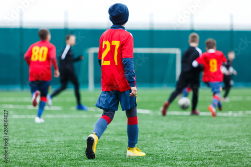 Boys kick soccer ball. Footballers run after the ball on green grass. Kids in white and red shirts dribbling, improve skills. Training, football, hobby, active lifestyle