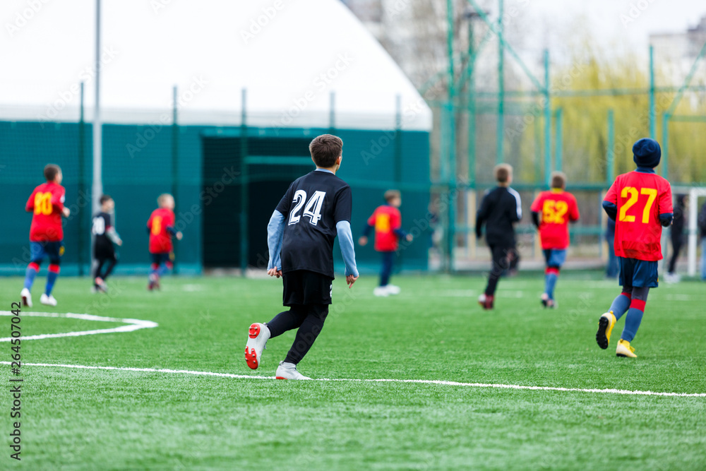 Obraz premium Boys at black red sportswear run, dribble, attack on football field. Young Soccer players with ball on green grass. Training, football, active lifestyle for kids