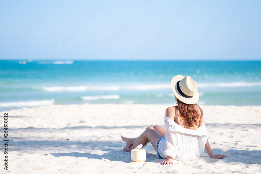 Fototapeta premium Portrait image of a beautiful asian woman enjoy sitting and drinking coconut juice on the beach