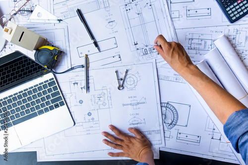 engineers pointing to building on blueprint and using laptop to drawing design building Project in office, construction concept. Engineer concept
