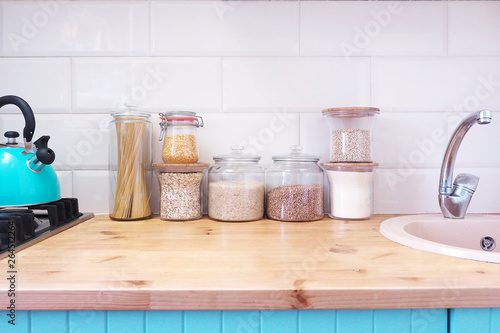 Glass jars with products. Blue kitchen with wooden top. Kettle on the stove..