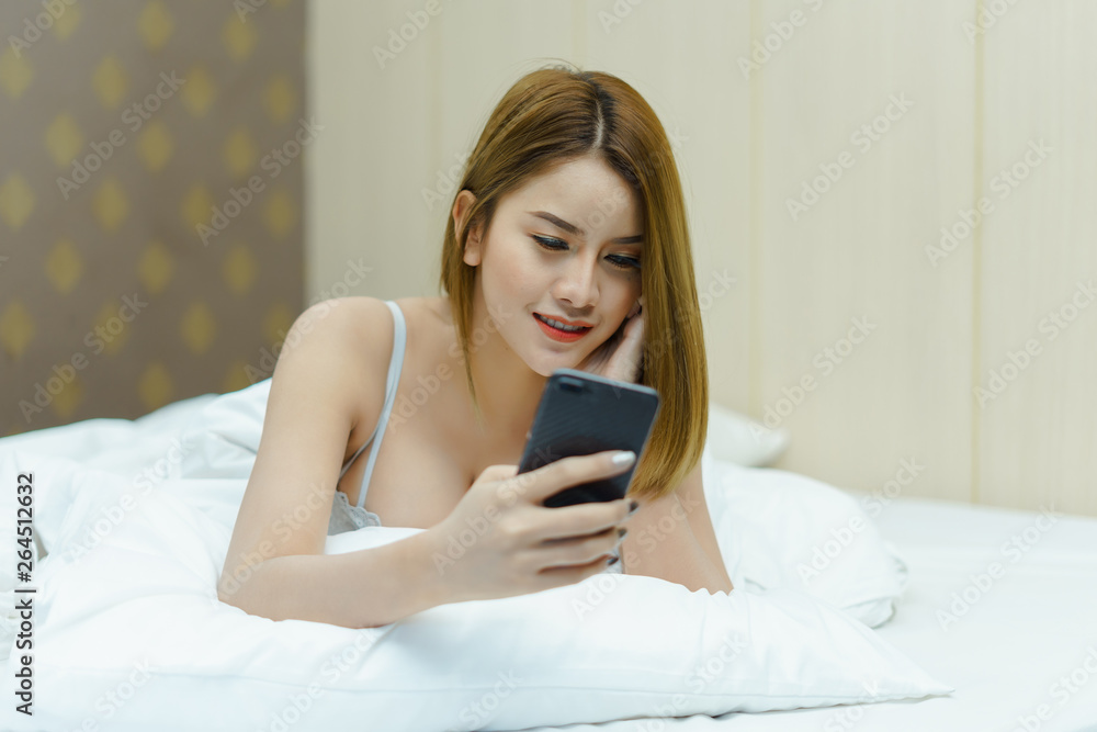 Young beautiful woman with long brown hair uses cell phone and relaxes on the white background bed. Young beautiful woman with long brown hair uses cell phone and relaxes on the white background bed.