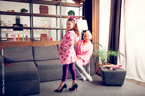 Fotografie Preschool girl posing in bathrobe and high-heeled shoes of granny