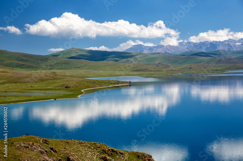 Beautiful view of the alpine lake. In the distance on a rocky hill stands a guy with a bicycle.