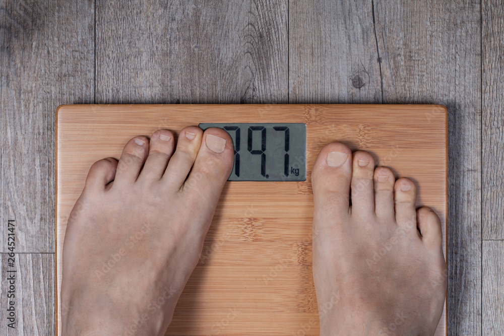 Legs of man standing on weight scale and his thumb covering display. Funny  weight concept. Stock Photo | Adobe Stock