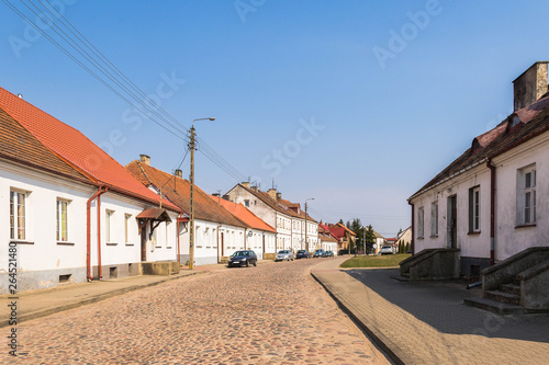Cityscape of historical Tykocin town in Poland. Old white painted houses with red color roofs alonside the old cobblestone street under the blue sky on a sunny day.
