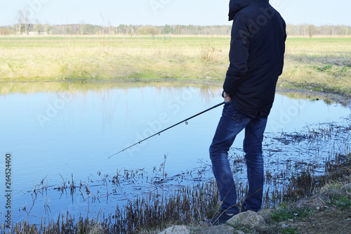 Man fishing with fishing rod on pond in cold spring day. Hobbies, recreation and leisure outdoor activities concept.