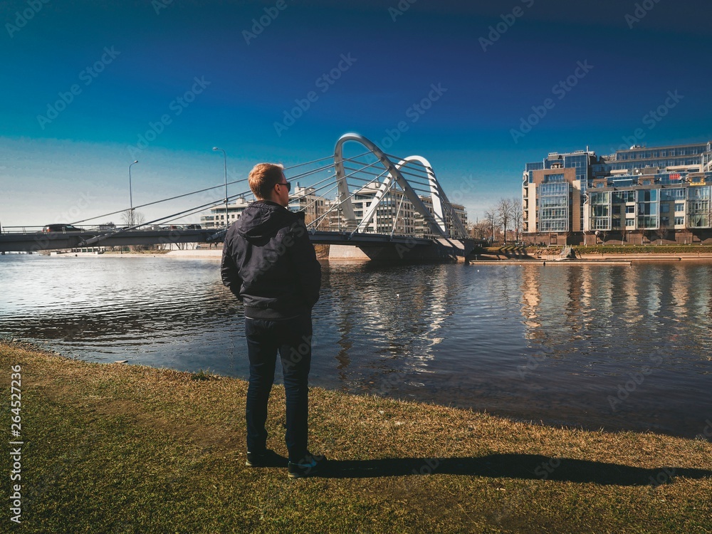 A blond man in a jacket stands against the background of Modern architectural design of a bridge in Saint Petersburg
