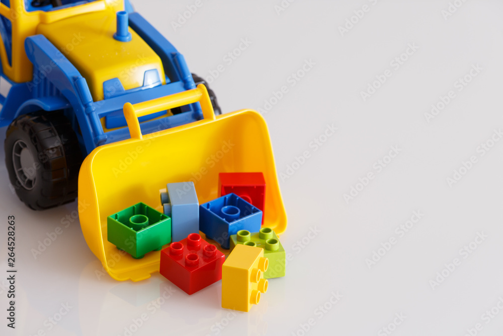Bright color toy bulldozer on a white table. Multi-colored tractor collects cubes in the bucket. Early development. Kids toys