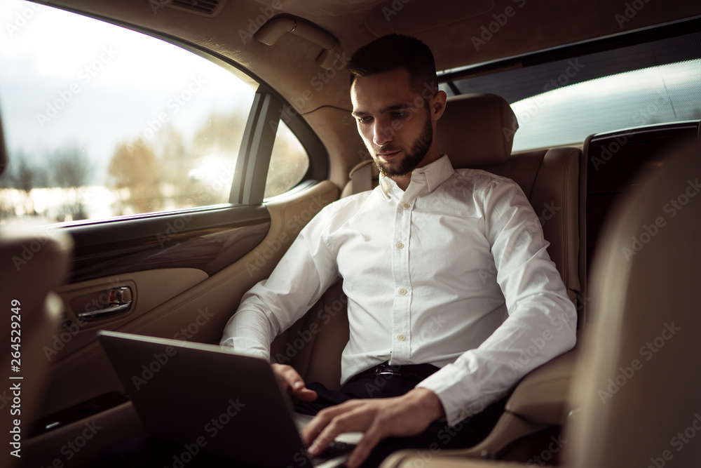 Man uses laptop sitting in back seat of car, businessman in taxi