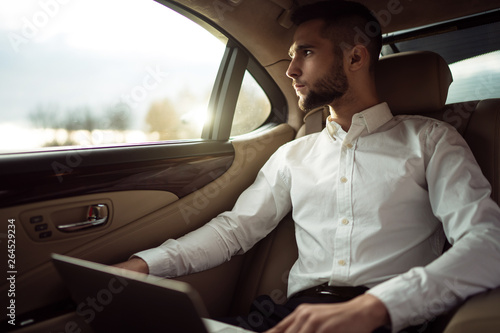 Man looking away while sitting on the back seat of a car, businessman in taxi © D'Action Images