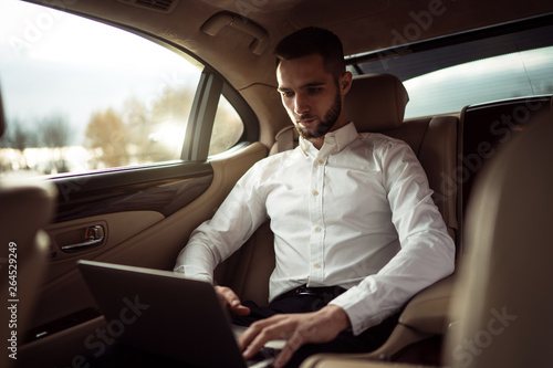 Man uses laptop sitting in back seat of car, businessman in taxi © D'Action Images