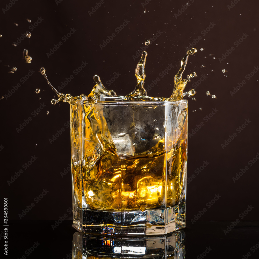 hexagonal glass of whiskey with ice and splashes from an abandoned and falling ice cube hexagonal glass of whiskey with ice and splashes from an abandoned and falling ice cube