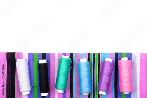 Sewing. Background of striped fabric and spools of threads of different colors on a white background. Flat Lay, space for text, Copy space, top view