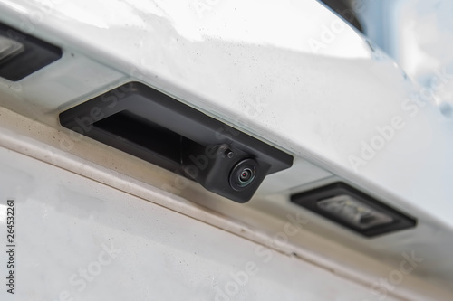 Black rear view camera with washer, car exterior. On white suv, license plate ceilings closeup