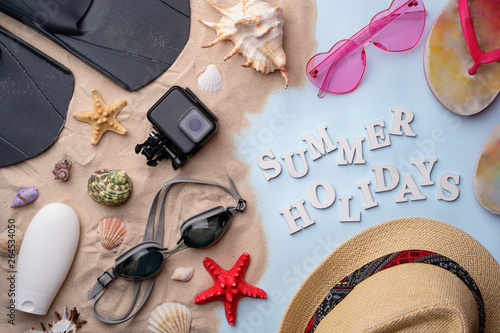 Swimming goggles, flippers, flip-flops, sunglasses, hat, sunscreen and action camera on sand
