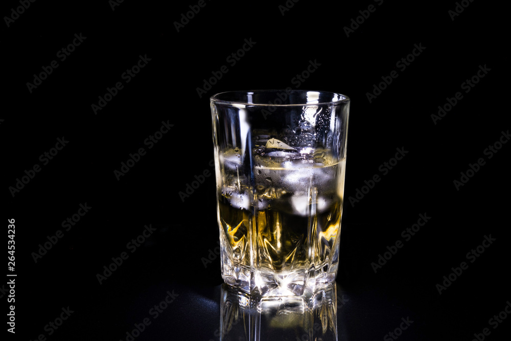 Cool glass of whiskey with ice covered with dew, stands on a black background