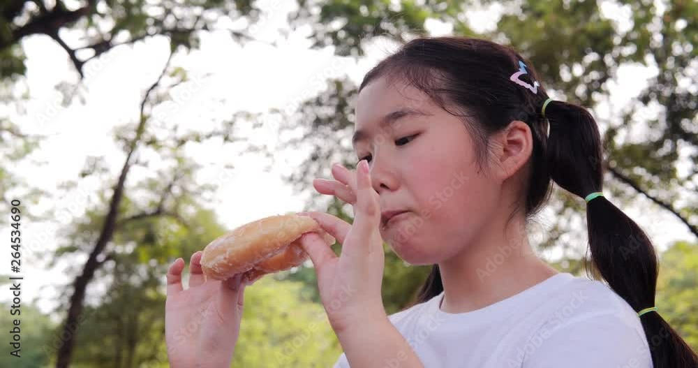 Asian little girl eating donut with happy emotion at park. Girl enjoy for eating donut alone. Asian little girl eating donut with happy emotion at park. Girl enjoy for eating donut alone.