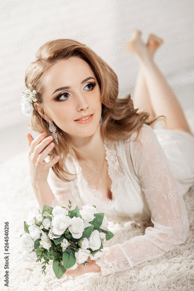 Beautiful girl with blond hair in a bright room is lying on the floor. Bride lying holding a bouquet