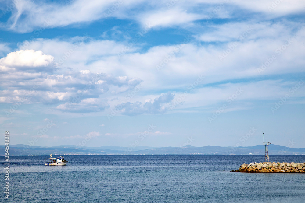 Small boat in blue sea approaching the harbor, tranquil blue sea with clouds in blue sky and fishing boat in summer, Halkidiki Greece