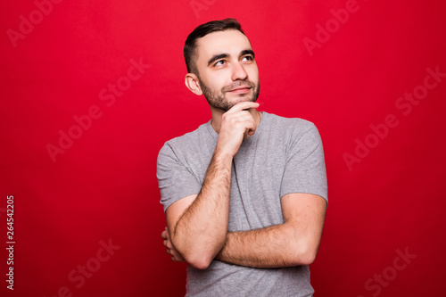 Handsome attractive young caucasian male expressing positive emotions holding hand under his chin isolated red bakground © F8  \ Suport Ukraine