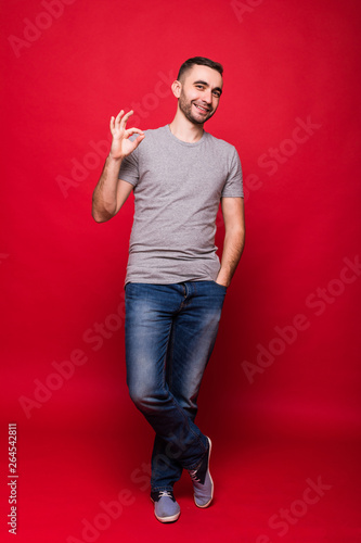 Portrait of handsome happy young man showing okay gesture standing isolated over red wall background. © F8  \ Suport Ukraine