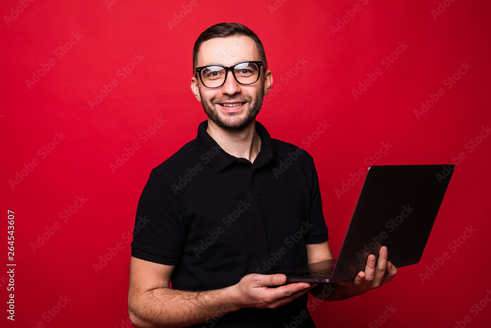 Young pretty man in glasses checking his laptop isolated on red background Young pretty man in glasses checking his laptop isolated on red background