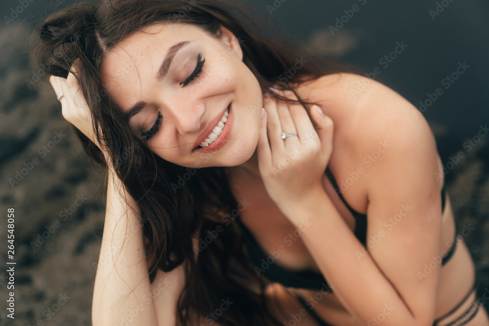 Portrait of happy girl with beautiful smile in swimsuit posing on black sand beach Portrait of happy girl with beautiful smile in swimsuit posing on black sand beach