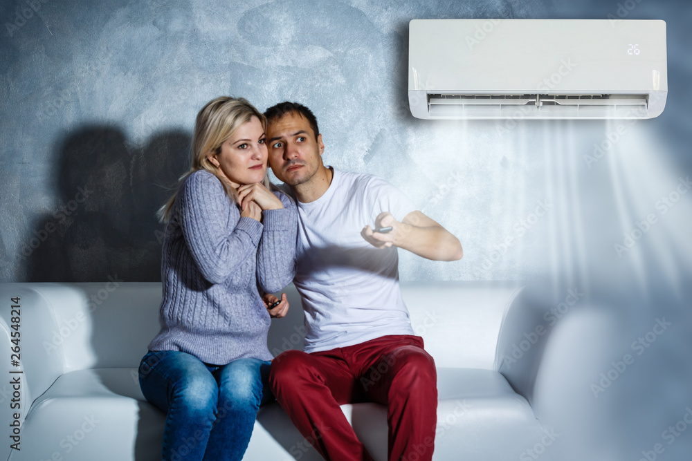 Naklejka premium couple turning on air conditioner during the summer heat while sitting on sofa
