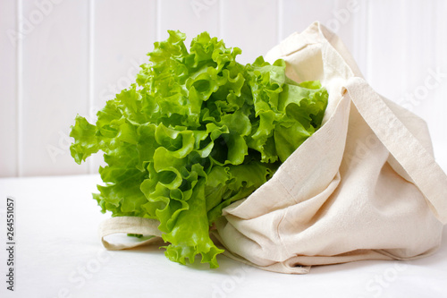 Fresh salad lettuce leaves in a linen shopping bag against a white wooden wall