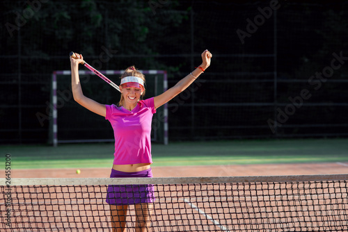 Happy female tennis player jumping near the net and laughing, celebrating her winning in tennis match. Sport, health care concept. © gorynvd